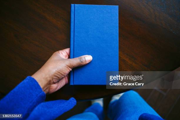 woman grabs book from table - blue wooden table stock-fotos und bilder