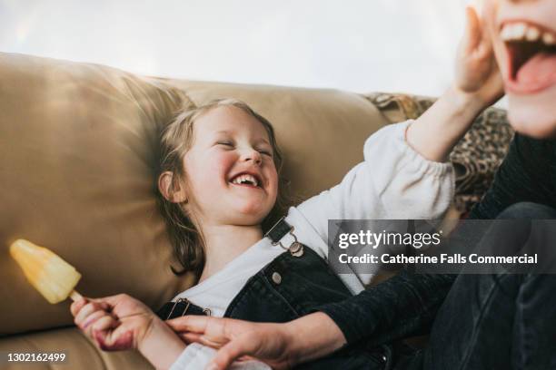 brother attempting to lick his younger sisters ice lolly as laughs and pushes him away - siblings stock-fotos und bilder