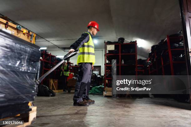 ein männlicher arbeiter mit handpalettenheber entlädt palettenware in einem lager - gummiband stock-fotos und bilder