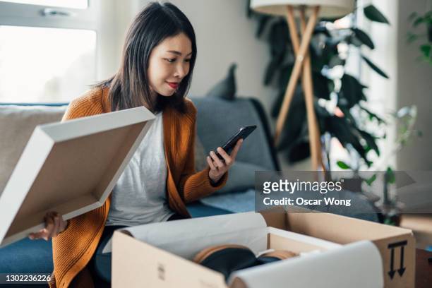 beautiful young woman with smartphone receiving parcel purchased online - compras em casa imagens e fotografias de stock
