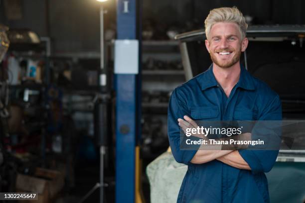young happy worker standing in auto repair shop with his arms crossed and looking at camera. - white jumpsuit stock pictures, royalty-free photos & images