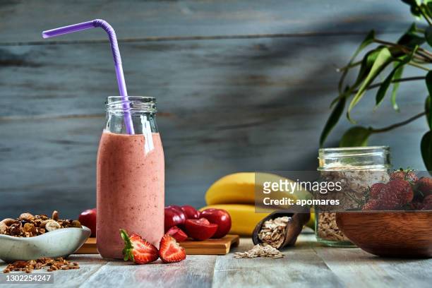 healthy food: banana and strawberry yogurt smoothie with cereal in bottle with straws on a rustic table. - strawberry milkshake stock pictures, royalty-free photos & images