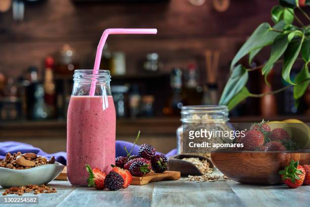 healthy food: banana and blackberry yogurt smoothie with cereal in bottle with straws on a rustic table. - strawberry smoothie stock pictures, royalty-free photos & images