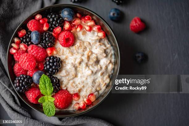 organic oatmeal topped with raspberries, blueberries, blackberries and pomegranate seeds and mint leaves - oatmeal stock pictures, royalty-free photos & images