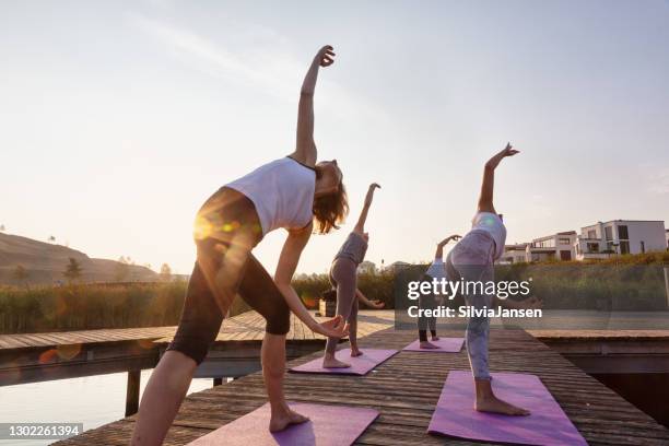 group of women exercising yoga on jetty in the city at sunrise - dortmund city stock pictures, royalty-free photos & images