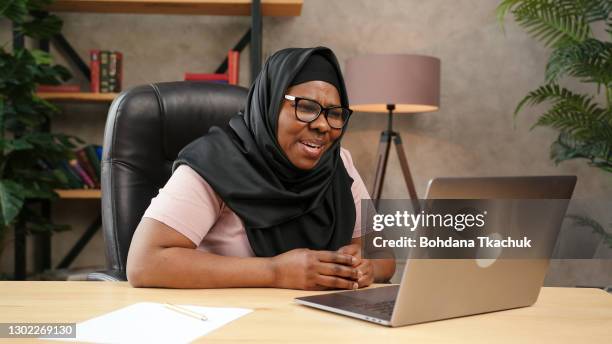 dame dodue dans les pourparlers noirs de hijab regardant dans l’affichage d’ordinateur portatif - voile religieux photos et images de collection