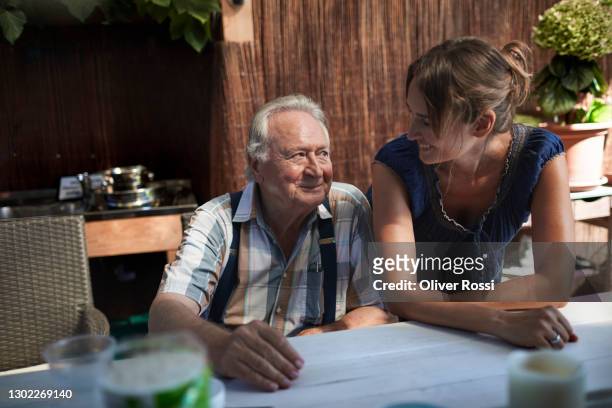 senior man smiling at adult daughter on garden patio - nur erwachsene stock-fotos und bilder