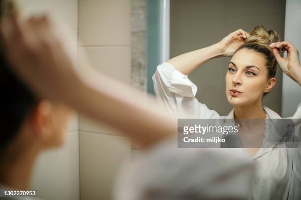 young woman doing hairstyle in mirror reflection - bun hair woman stock pictures, royalty-free photos & images
