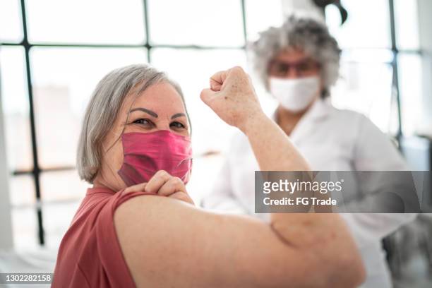 woman being vaccinated and flexing biceps muscle - wearing face mask - covid 19 safety stock pictures, royalty-free photos & images