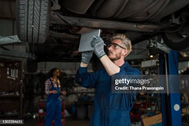 mechanic examining underside of car - undercarriage stock pictures, royalty-free photos & images