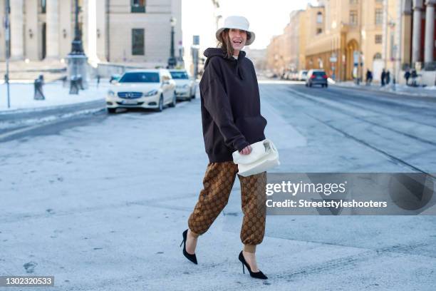 Influencer Annette Weber wearing vintage camel colored GG trackpants by Gucci, black pumps by Jimmy Choo, a dark grey hoodie by H&M, a white bucket...