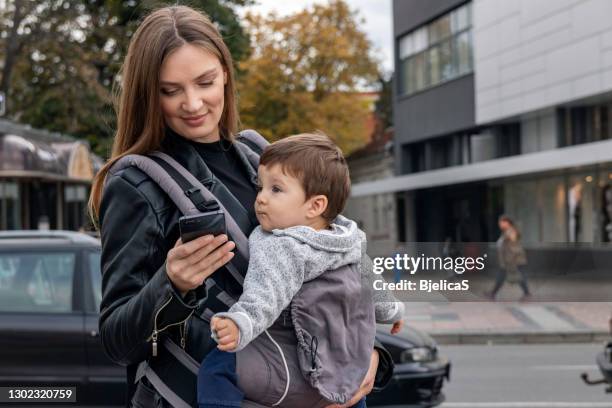 mother using smart phone while waiting a cab with her baby boy in baby carrier - taxi boys stock pictures, royalty-free photos & images