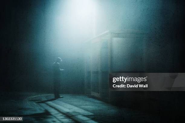 a moody hooded figure, standing by a bus stop looking at his phone on a foggy winters night. with a grunge, artistic, edit - crime fotografías e imágenes de stock