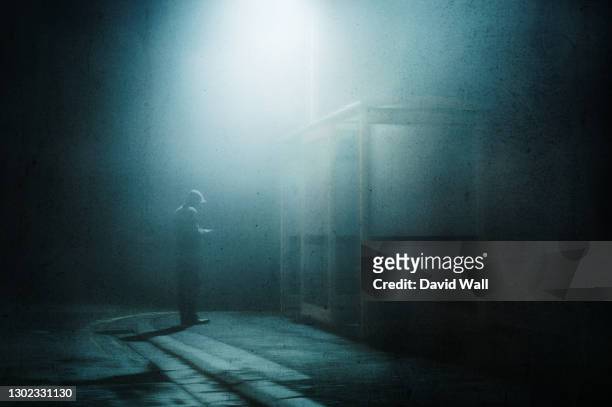a moody hooded figure, standing by a bus stop looking at his phone on a foggy winters night. with a grunge, artistic, edit - hotelse bildbanksfoton och bilder