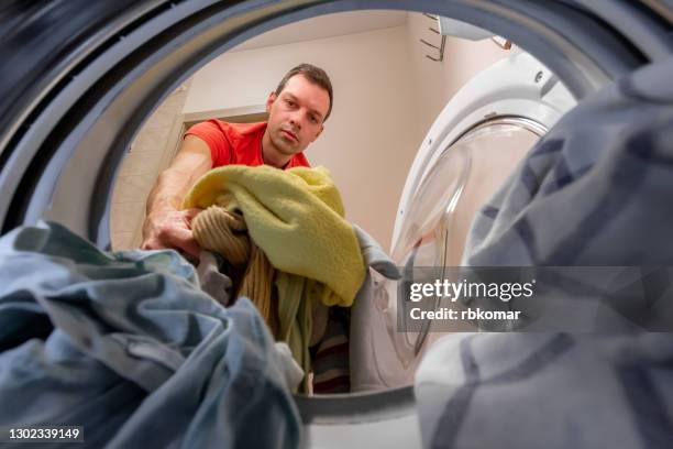 a man loads a pile of dirty clothes into the drum of the washing machine for cleaning. household routine and apartment cleaning - smelly laundry stock pictures, royalty-free photos & images