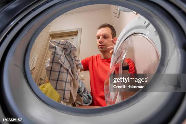 portrait of a serious young man doing dirty laundry in a laundromat - remove clothes from 個照片及圖片檔