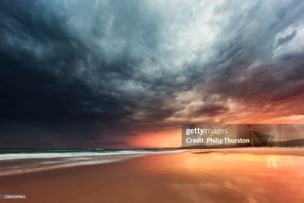 Tidal retreat reflecting dramatic storm on the beach at sunset