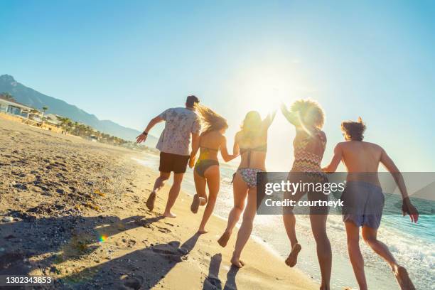 gruppe von freunden laufen und springen in den ozean bei sonnenuntergang. - summer spain stock-fotos und bilder