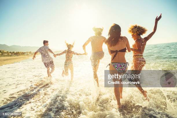 group of friends running and jumping into the ocean at sunset. - cinco pessoas imagens e fotografias de stock