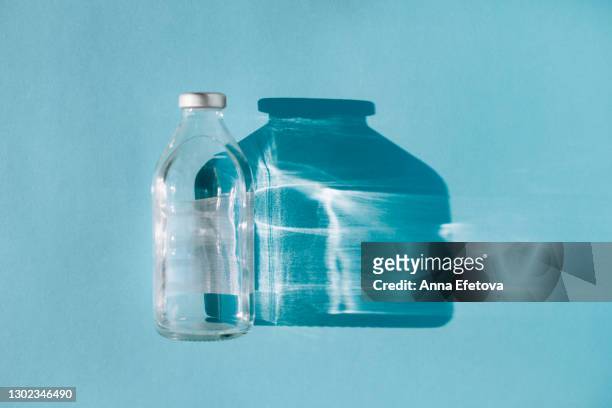 bottle with saline on blue background with shadow and illuminating reflections. covid-19 fighting concept - infused water stockfoto's en -beelden