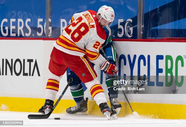 Elias Lindholm of the Calgary Flames pins Loui Eriksson of the Vancouver Canucks along the side boards during NHL hockey action at Rogers Arena on...