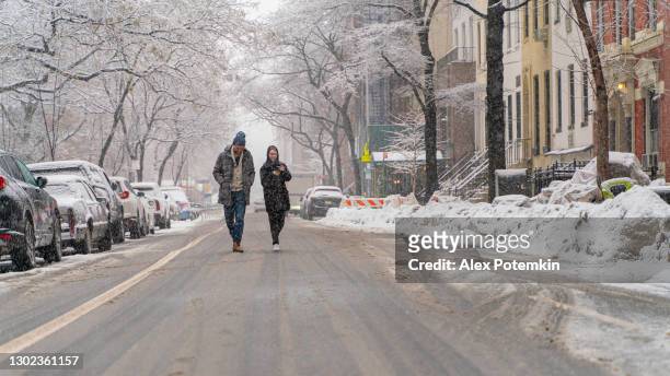 young happy friends walking in the middle of the empty street of the deserted city during the heavy snowfall. - new york city snow stock pictures, royalty-free photos & images
