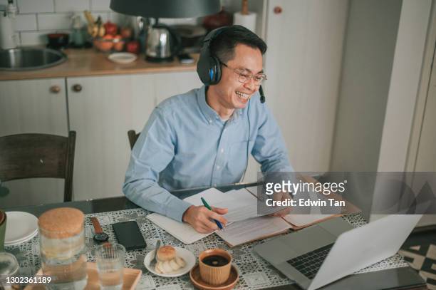 asian chinese mid adult man smiling attending online meeting using laptop at dining area with headphone headset - working on laptop in train top view stock pictures, royalty-free photos & images