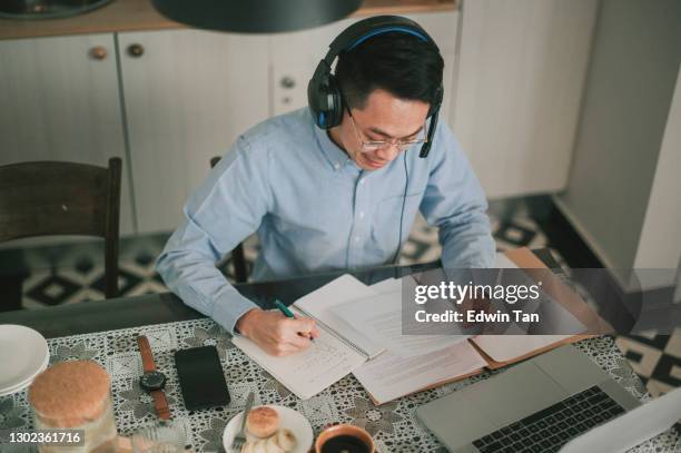 asian chinese mid adult man smiling attending online meeting using laptop at dining area with headphone headset - working on laptop in train top view stock pictures, royalty-free photos & images