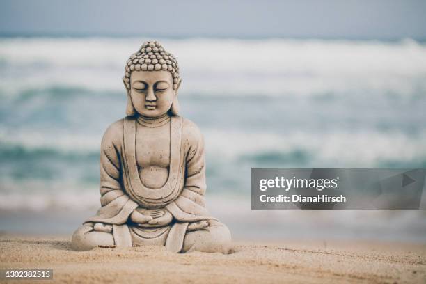 näring av en buddha stenfigur som sitter på stranden framför det något grova havet - buddha bildbanksfoton och bilder