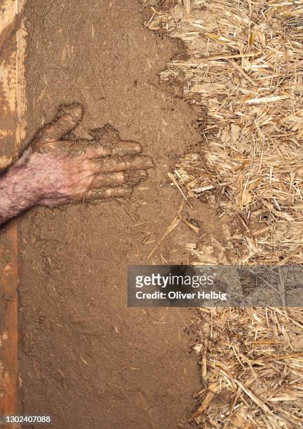a caucasian man's hand evenly smears clay on a straw wall. - rohbau haus stock-fotos und bilder