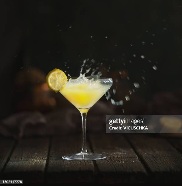 yellow lemon limoncello liqueur cocktail with splash drops at dark background. - splashing cocktail stock pictures, royalty-free photos & images