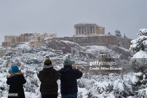 People take photos of The Parthenon temple atop the Acropolis hill archaeological site during a heavy snowfall in Athens on February 16, 2021 in...