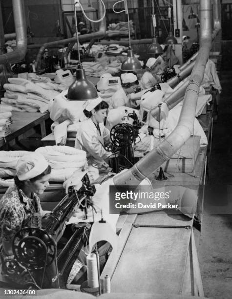 Women factory workers using Singer Sewing machines manufacture asbestos fire protection suits for the Royal Air Force and Fleet Air Arm fire fighting...