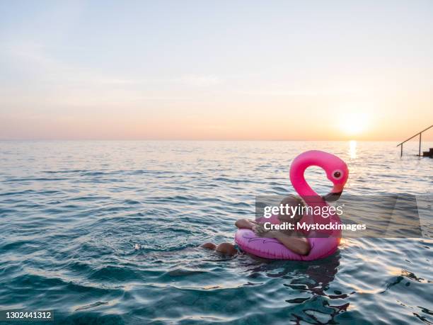 woman watches sunrise while swimming with inflatable flamingo - plastic flamingo stock pictures, royalty-free photos & images