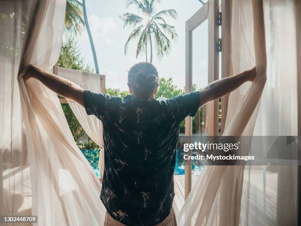 mann öffnet vorhänge im hotelzimmer bei sonnenaufgang - curtain hotel stock-fotos und bilder