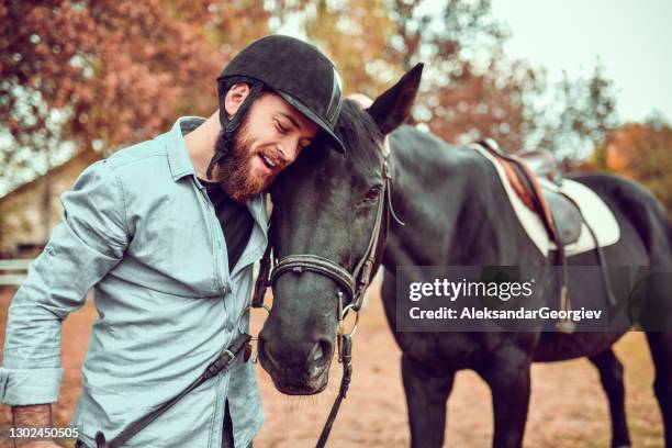 moderne männliche jockey umarmung pferd nach spaß tag reiten auf ranch - saddle stock-fotos und bilder