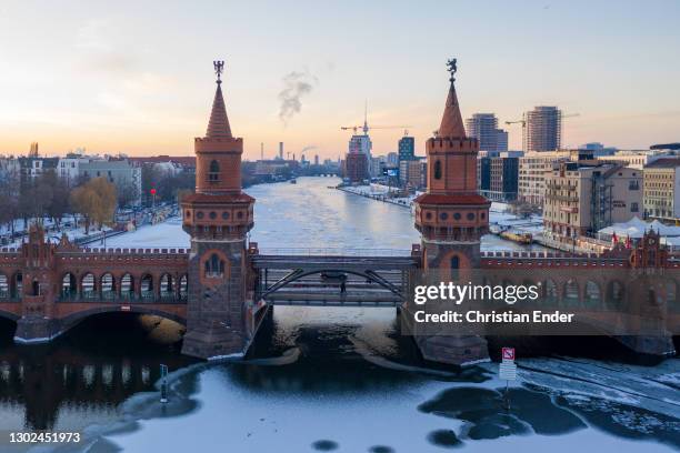 In this aerial view the Oberbaumbruecke bridge stands on frozen Spree River between Friedrichshain district and Kreuzberg district at sunset on...