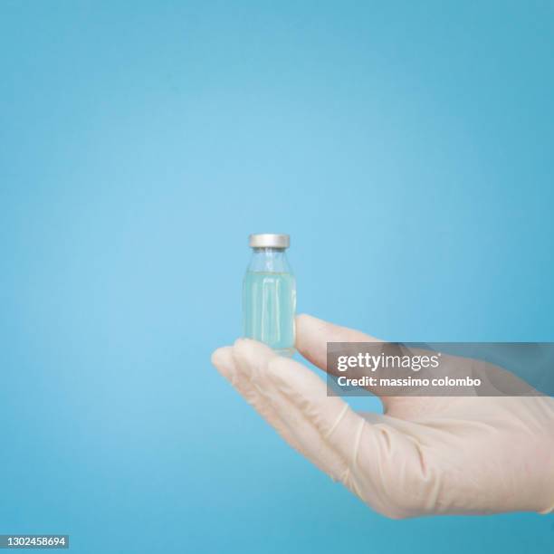 hand in surgical gloves, vial covid-19 vaccine without label, isolated on light blue background - blauer handschuh stock-fotos und bilder