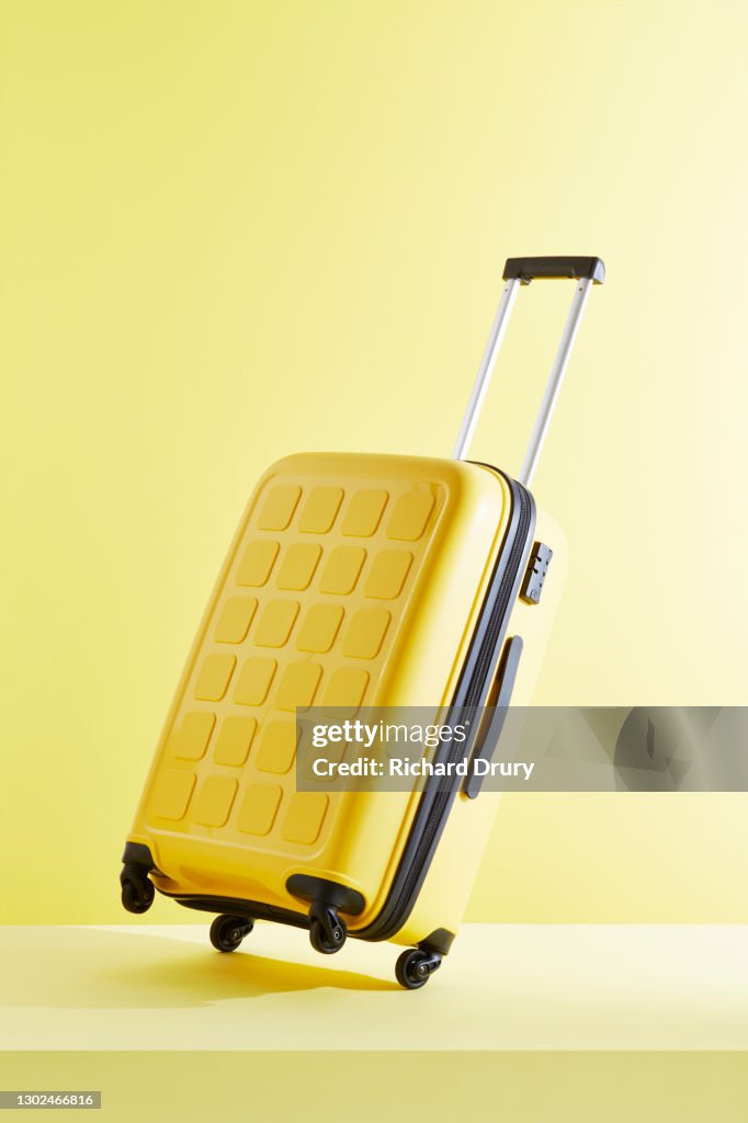 A tilted yellow suitcase on a yellow background