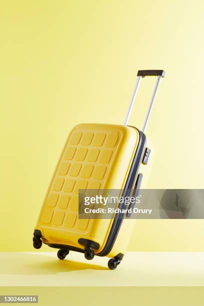 a tilted yellow suitcase on a yellow background - suitcase stock pictures, royalty-free photos & images