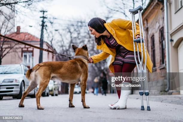 frau mit krücken streichelhund - gehgips stock-fotos und bilder