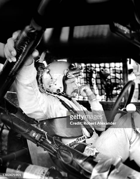 Driver Dale Earnhardt Sr. Sits in his race car while undergoing repairs to wreck damage suffered during the running of the 1981 Firecracker 400 stock...
