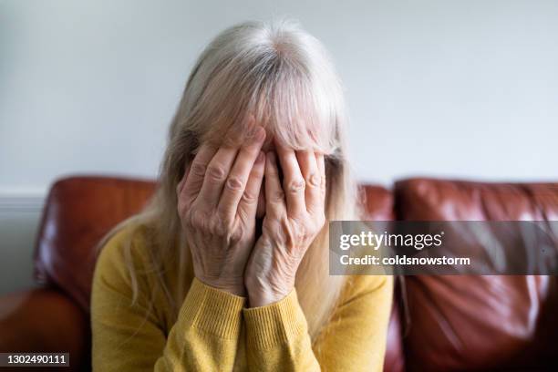 gedeprimeerde hogere vrouw met overhandigingsgezicht thuis - mishandeling stockfoto's en -beelden