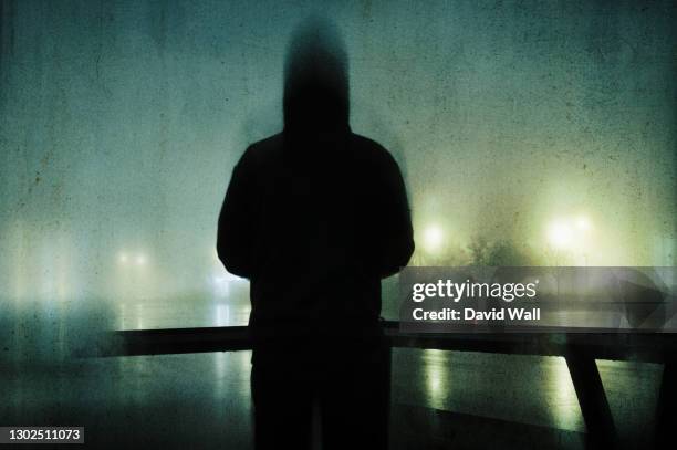 a spooky hooded figure. standing by a river in a city on a foggy winters night. with a grunge, artistic, edit - threats fotografías e imágenes de stock