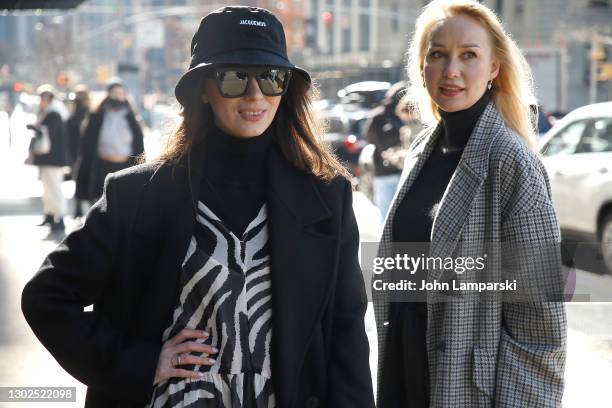 Woman wearing a zebra print suit under a black coat poses with a woman in a plaid coat and a black turtle neck arrive at Spring Studios during New...