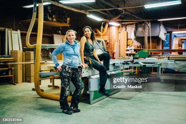 portrait of smiling colleagues by machinery in workshop - wood worker posing stock-fotos und bilder