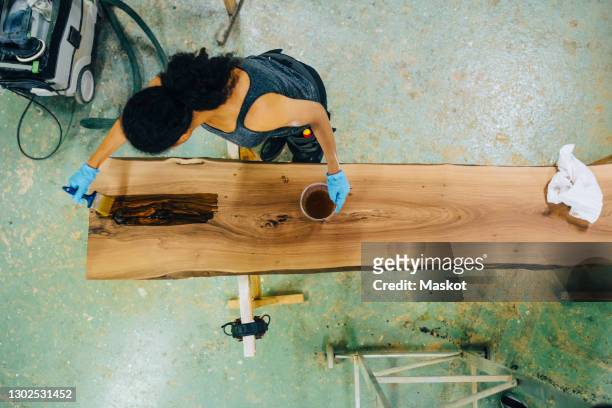 high angle view of craftswoman painting wooden plank in workshop - snickeriarbete bildbanksfoton och bilder