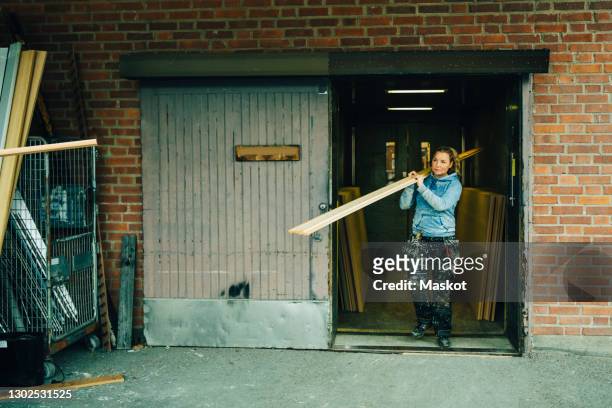 craftswoman carrying plank on shoulder in workshop - carrier stock pictures, royalty-free photos & images