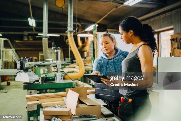 female carpenters discussing over digital tablet during meeting in workshop - schreiner tablet stock-fotos und bilder