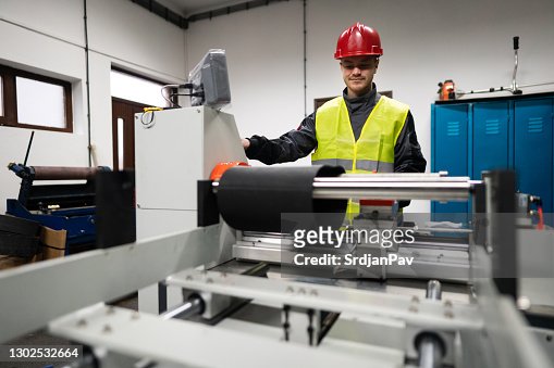 Young male factory worker working on the machine for rolling rubber compounds